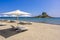 Deck chair and umbrella on beautiful Agios Stefanos Beach in front of paradise Island Kastri- historical ruins and paradise