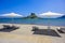 Deck chair and umbrella on beautiful Agios Stefanos Beach in front of paradise Island Kastri- historical ruins and paradise