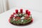 A decorated advent wreath with candles lies on a white table