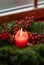 Decorated Advent wreath from fir branches with red burning candle on a wooden windowsill in the time before Christmas