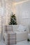 Decorated Christmas tree behind white sofa with plaid and cushion. Happy new year inscription on wall, vertical shot