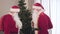 Decorated Christmas tree standing indoors as two Santas coming. Side view of surprised Santa Clauses meeting on New Year