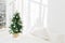 Decorated festive Christmas tree in white classic bedroom interior with soft bed. Winter home interior. Cozy season. New Year,