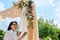 Decorating arch with textiles with flowers and plants. Woman organizer, owner, with digital tablet near wedding arch