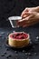 Decorating homemade pie. Woman hands pouring icing sugar on open red berry pie on black background high angle view