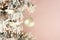 Decoration on Christmas tree - white birds and silver ball on snowy spruce on light pink background. Closeup