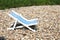 A decoration toy striped beach chair for sunbathing and relaxing stands on a stones beach a hot sunny day, side view