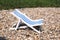 A decoration toy vintage striped beach chair for sunbathing and relaxing stands on a stones beach a sunny day, side view