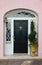 Decorative cut glass windows and pink stucco walls frame a black wooden door with an ornamental brass knocker