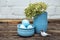 Decorative dyed easter eggs in blue pot with green hydrangea in skyey ceramic vasa and a little bird on brown wooden background