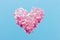 Decorative heart shape made of pink sequins on an isolated blue background.