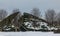 The decorative hill in the winter city park is covered with evergreens.