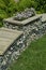 Decorative pebble gabion landscaped with a bench and plants in an urban green space