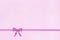 Decorative shiny ribbon with bow on pink background.