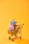 Decorative shopping trolley with presents on bright orange background.