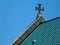 decorative stone church cross at top of sloped green copper roof. closeup view.