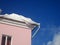 Decorative white snowdrift on the roof of a pink house and blue sky