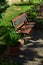 Decorative wooden bench with smithcraft on backrest, placed on tiled floor near cultivated lawn and flower pots