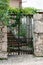 Decorative wrought iron front yard entrance doors mounted on traditional stone wall covered with crawler plant and fig tree leaves