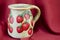 Decoupage decorated strawberry pattern pitcher on red fabric bac