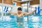 Dedicated elderly caucasian woman in striped swimsuit and black hair cap using pool buoys to do aqua exercised. Swimming