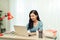 Dedicated female freelancer in glasses and wireless headphones smiling at camera while sitting at laptop with mug