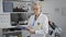 Dedicated senior grey-haired scientist woman, in lab coat, taking intricate notes at center\\\'s laboratory amidst science research