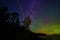 Deep blue and violet night sky with water and green and orange glow of aurora lights with tree silhouettes