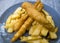 Deep fried battered strips of fish fillets on top of a serving of potato fries