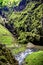 A deep gorge overgrown with vegetation with a small river