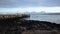 Deep open fjord landscape with mighty snowy mountain range in the background and long old rock and wood pier