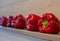 Deep red bell peppes lined up on a shelf in front of a white painted wall.