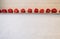 Deep red bell peppes lined up on a shelf in front of a white painted wall.