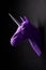Deep shadowed violet unicorn`s head profile hanging on contrast wall.