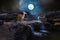 The deer stands on a small waterfall in the middle of the rocky rapids to drink at night with the big moon and moonlight.