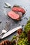 Deer or venison steak with ingredients like sea salt, herbs and pepper and cutlery, food background for restaurant or hunting lovi