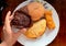 Deferent variety of snacks display on a plate a hand is holding chocolate muffin