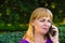 Defocus close-up caucasian blond woman talking, speaking on the phone outside, outdoor. 40s years old woman in purple