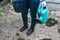 Defocus close-up gardener is standing on a beds. The farmer holding green watering can an black bucket. Greens. Gardening and