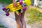 Defocus girl holding yellow penny board. View from back. Summer bright colors. Child hands holding short cruiser