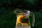 Defocus glass jug of lemonade with slice lemon and mint on natural green background with water drops. Pitcher of fresh