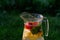 Defocus glass jug of lemonade with slice lemon and mint on natural green background with water drops. Pitcher of fresh