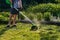 Defocus grass trimmer. A man mowing the grass. Outdoor view of young worker using a lawn trimmer mower cutting grass in