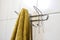 Defocus mustard towel hanging on hook. Metal sticky towels hanger for bathroom tiled wall. Closeup mustard towel hanging