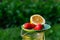 Defocus saucer with lemon and two strawberry standing on glass jug of lemonade on nature green background. Summer fruits