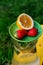 Defocus saucer with lemon and two strawberry standing on glass jug of lemonade with slice lemon and leaves of mint on