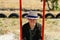 Defocus smiling young woman in checkered shirt and hat swinging on swing on playground. Hipsters and hippie portrait