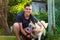 Defocus young caucasian man smiling and seating with dog. The portrait of a guy squatting near the siberian laika husky