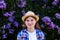 Defocus young flower woman. Beautiful woman in checkered shirt and hat with lilac bunch and meadow of flowers in spring