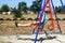 Defocus young man swinging on swing on playground. Countryside area. Bright blue and red swing. Kids summer game. Guy